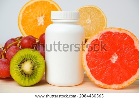 Vitamins. White container for vitamins on a background of fruits. Citrus, lemon, orange, grapes.
