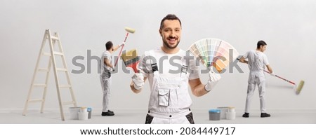 House painter holding a color swatch palette and a brush and other painters painting a wall isolated on white background