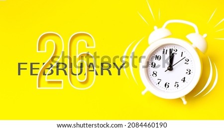 February 26th. Day 26 of month, Calendar date. White alarm clock with calendar day on yellow background. Minimalistic concept of time, deadline. Winter month, day of the year concept