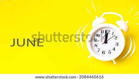 June. Month, Calendar month. White alarm clock with calendar day on yellow background. Minimalistic concept of time, deadline. Summer , month of the year concept