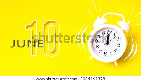 June 10th. Day 10 of month, Calendar date. White alarm clock with calendar day on yellow background. Minimalistic concept of time, deadline. Summer month, day of the year concept