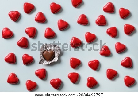 Romantic red chocolate sweets as heart in red foil and one open sweet on blue background. Valentine's day greeting card. Love concept.