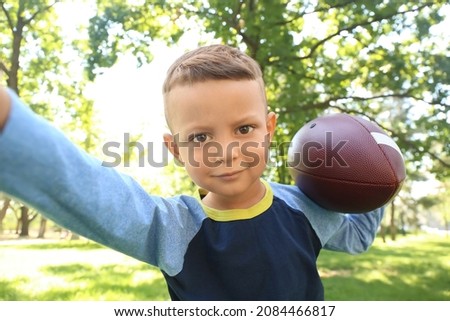 Little boy with rugby ball taking selfie outdoors