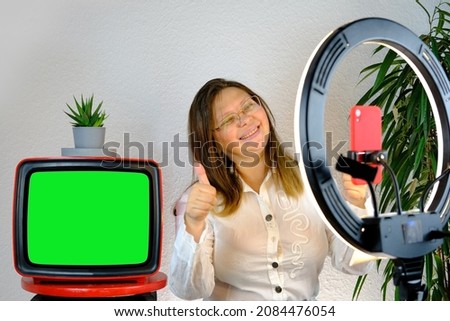 woman 40-45 years old, pretty female blogger sits in front of ring light and red smartphone, emotionally talks on topic of business, hobby during quarantine covid 19, old TV with green screen