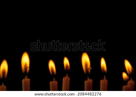 Blurred image of a group of candles, front view with the light of beautiful bright yellow golden flames on black background. Ideas for Halloween, Christmas, Home, Romance, Love, Copy space for you.
