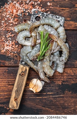 Raw Headless tiger shrimps prawns on a butcher cleaver. Dark wooden background. Top view