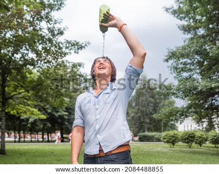 Laughing man douses himself with water from bottle. Staying cool in summer. Wet fun in urban park. Sincere emotions. Candid lifestyle. Royalty-Free Stock Photo #2084488855