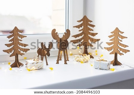 Christmas deer. Decorative golden gift box and wooden reindeer toy on white windowsill at home. Happy new year 2022. Handmade figure deer and fir tree. Eco style diy.