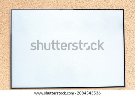 White blank advertising sign with black frame hanging outside at the exterior wall of a building
