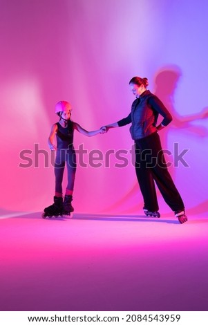 child skater athlete holding hands of her trainer, training for competition, photo on pink background in a studio