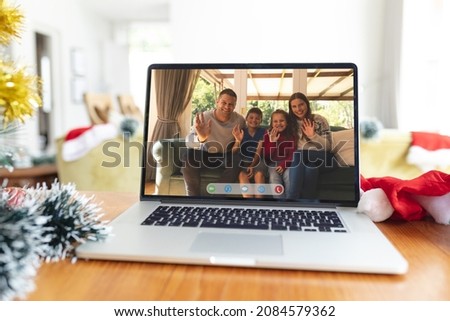 Happy caucasian family waving on laptop video call screen at christmas time. christmas, festivity and communication technology.