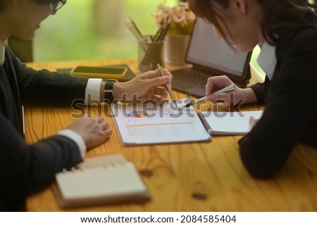 Photo of young businesspeople working together at the wooden working desk with a digital tablet and clipboard.