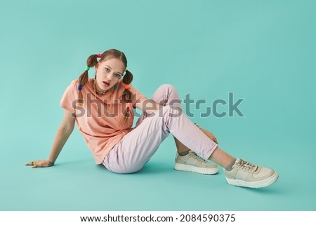Teen girl with creative hairstyle looking at camera with serious expression while sitting
