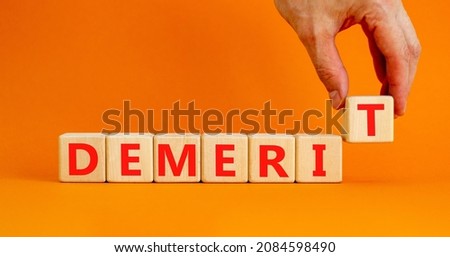 Demerit symbol. The concept word Demerit on wooden cubes. Beautiful orange table, orange background, copy space. Businessman hand. Business and demerit concept.