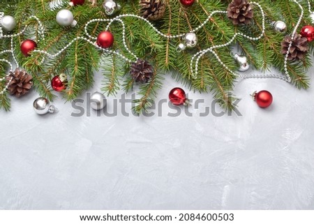 Christmas composition with red glass balls. The branches of the Christmas tree are decorated on a gray background.