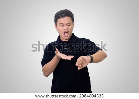 Portrait of shocked Asian man in black polo shirt looking at his wrist watch, coming late for meeting. Advertising concept. Isolated image on white background