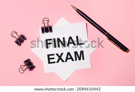 On a light pink background, black paper clips, black pen and white note paper with the words FINAL EXAM. Flat lay
