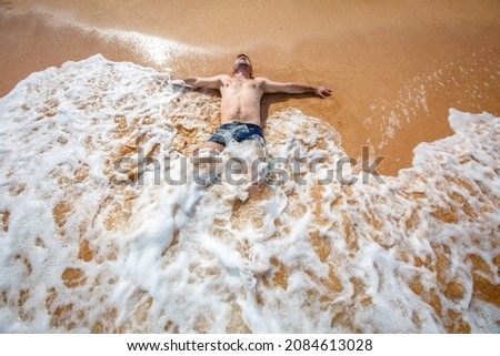 A handsome young man lying in the clear water at the beach seashore Royalty-Free Stock Photo #2084613028