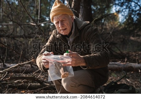 Senior man singing transparent plastic bag while picking mushrooms