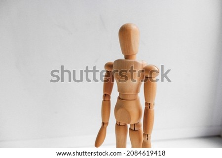 A wooden figure of a man standing on a white table.  Hand gestures pointing in different directions. Traffic controller.