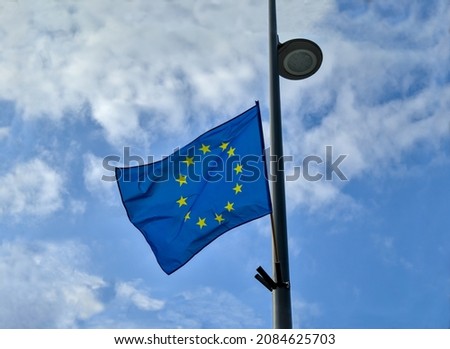 European Union flag standing on a street light pole and fluttering in the wind. Dramatic cloudy sky in the background