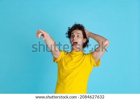 Emotive portrait of young excited man in yellow T-shirt pointing somewhere isolated over blue background. Concept of feelings, youth, fashion, facial expression, emotions, lifestyle, ad