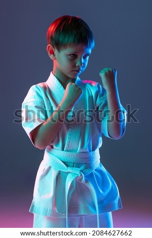 Portrait of child, concentrated sportsman training, practising karate isolated over gradient blue background in neon. Concept of martial art, healthy lifestyle, sport, action, combat sport and ad Royalty-Free Stock Photo #2084627662