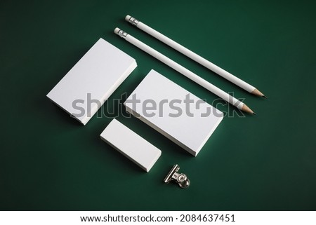 Blank stationery set. Photo of blank business cards, pencils, eraser and clip on green background.