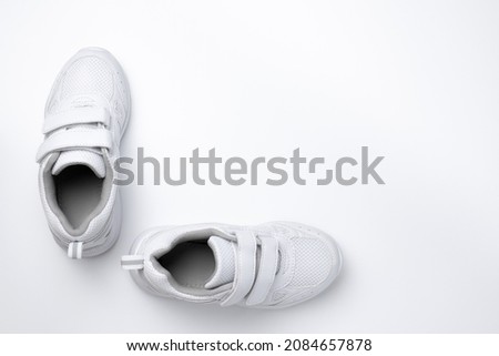flat lay two white unisex sneakers with velcro fasteners at a 90 degree angle to each other isolated on a white background.