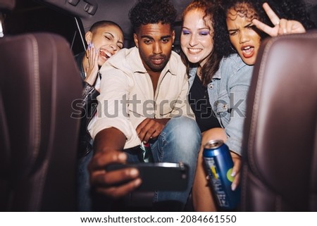 Diverse group of friends taking a selfie together inside a car. Group of young friends posing for a group photo in front of a camera phone. Carefree friends taking a ride home after a party.