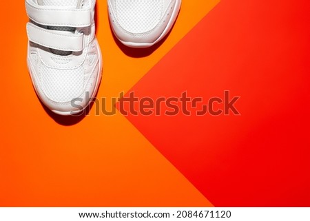 top view the front parts of two white sports shoes in the corner on an abstract geometric paper orange and red background with copy space.