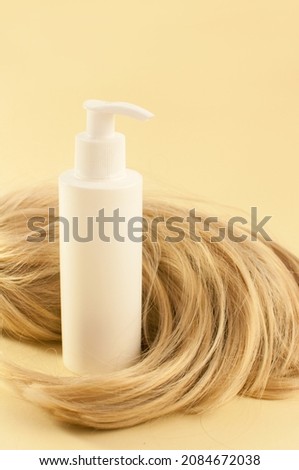 a white tube with a dispenser next to the blonde's hair on a beige background Royalty-Free Stock Photo #2084672038