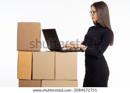 Woman entrepreneur. Business owner on light background. Girl with laptop and boxes. Businesswoman woman prints text. Business owner is engaged in order fulfillment. Successful lady in black dress