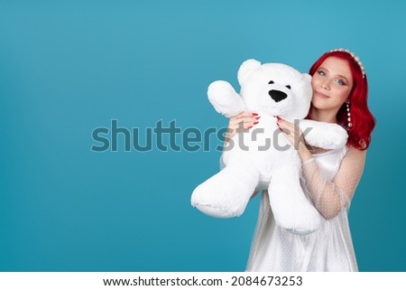 close-up a beautiful smiling woman in a white dress presses a large white teddy bear to her face , isolated on a blue background.