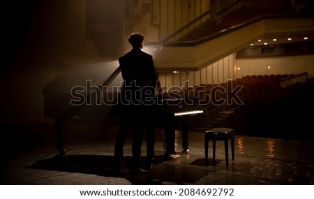 Young aspiring musician standing near grand piano on a stage of a huge concert hall