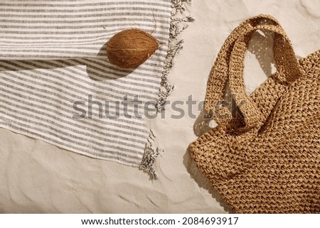 Striped linen beach towel with fringes, woven bag and coconut on sandy beach with shadows from palm tree. Relaxation and tropical summer holidays concept Royalty-Free Stock Photo #2084693917