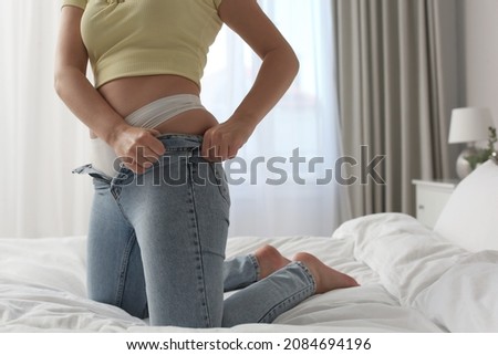 Woman trying to squeeze into tight jeans on bed at home, closeup Royalty-Free Stock Photo #2084694196