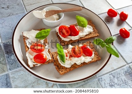 Gluten Free Organic Tomato Crackers with Lactose free Spread and fresh Tomatoes  on ceramic tile background.