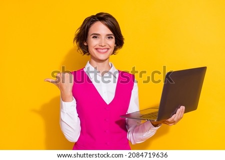 Portrait of attractive cheerful girl holding in hand laptop showing copy space isolated over bright yellow color background