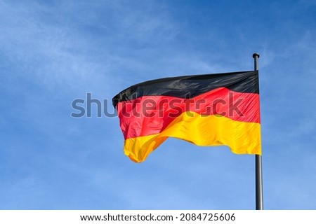 German flag flying on the wind. Waving flag of Germany on flagpole against blue sky. Deutschland. Black, red and yellow colors on German flag in a front of Bundestag.