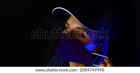 woman removes a medical mask in blue rays of neon light on a black background. Horizontal banner