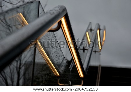from the bottom of the handle is a recessed LED strip with a yellow light. the side of the stair railing is made of glued glass panels without frames. stainless steel railing bars on metal handles Royalty-Free Stock Photo #2084752153
