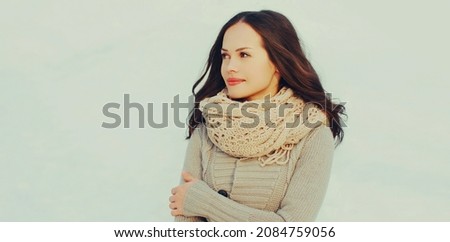 Portrait of beautiful young brunette woman looking away wearing a knitted scarf, sweater outdoors