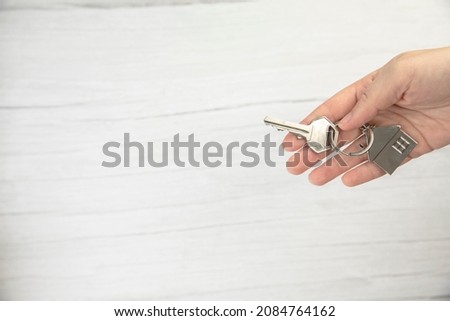 realtor female hand holding new door key to new house on white background top view with copy space, buying new home concept space for text