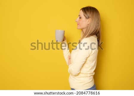 Profile picture young woman drinking cup of coffee isolated over yellow background.
