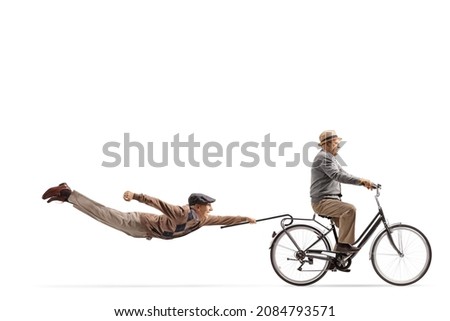 Elderly man riding a bicycle and other man flying behind isolated on white background Royalty-Free Stock Photo #2084793571