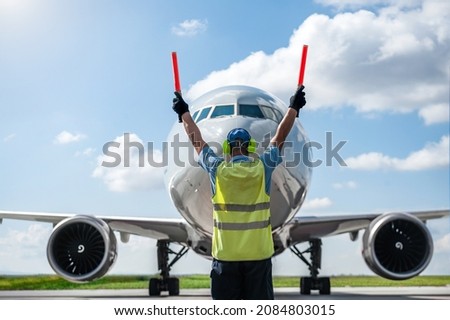 Ground Crew in the signal vest. Aircraft is taxiing to the parking place. Royalty-Free Stock Photo #2084803015