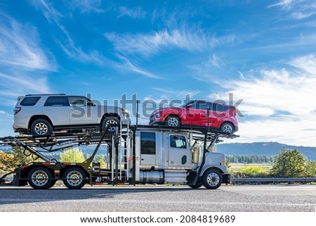 Industrial powerful white big rig car hauler semi truck transporting cars on two level modular semi trailer running on the winding road with dry grass and autumn forest on the hill
 in Columbia Gorge Royalty-Free Stock Photo #2084819689