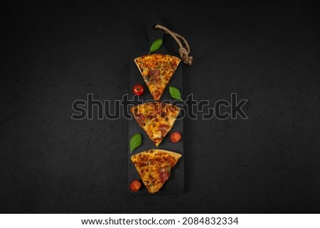 Three slices of pizza, cherry, basil on a black wooden cutting board with a red striped kitchen napkin lies in the center on a black background with copy space on the sides, top view close-up.