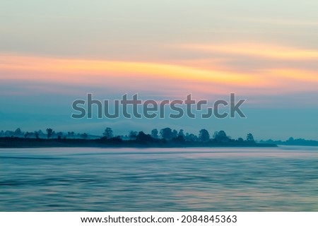 long exposure photography creates motion of cloud, lake surface, in beautiful orange sky at dawn before  sunrise and reflection of light on the lake surface With haze, smoke effect.